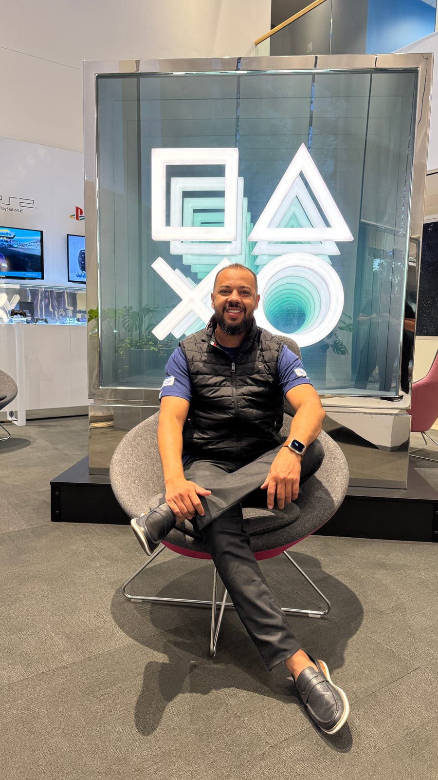 Gleidson Andrade em um espaço de experiência da PlayStation, da Sony, com os símbolos icônicos do console ao fundo