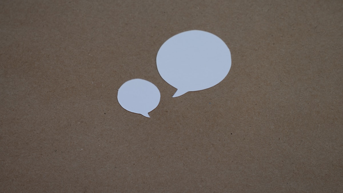 Dois balões de fala em papel branco sobre uma superfície de madeira, simbolizando a conversa entre a pessoa e a inteligência artificial