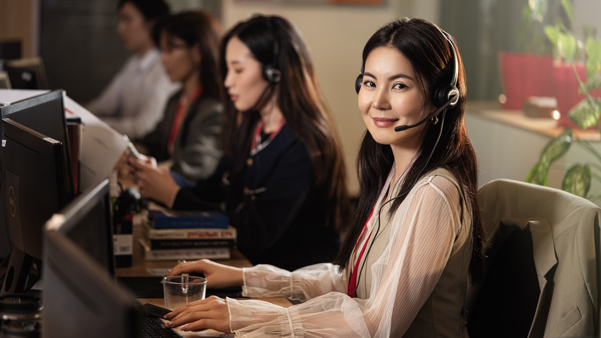 Atendente sorrindo usando um headset em frente ao computador